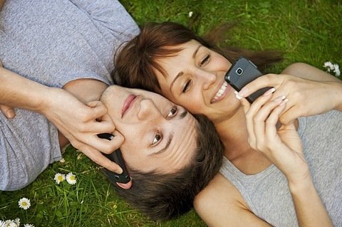 Парень и девушка лежат на траве и разговаривают по мобильным телефонам